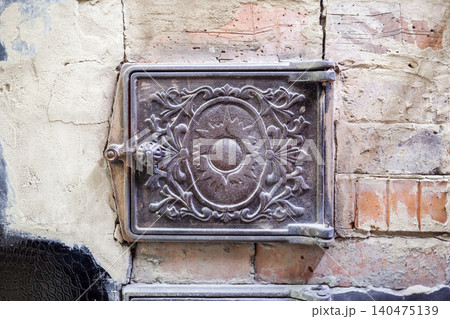 A decorative cast iron cover is mounted on a weathered brick wall, revealing intricate designs that reflect historical craftsmanship in an urban environment. A decorative cast iron cover is mounted on a weathered brick wall, revealing intricate designs that reflect historical craftsmanship in an urban environment. 140475139
