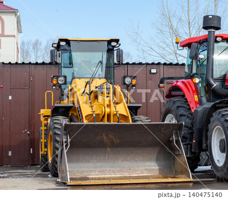 Heavy machinery including a yellow loader and a red tractor is parked at a construction site under clear skies, showing industrial activity. 140475140