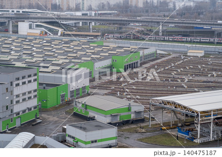 A view of a city area showing warehouses with green walls and storage spaces next to a rail yard with tracks in use. A view of a city area showing warehouses with green walls and storage spaces next to a rail yard with tracks in use. 140475187
