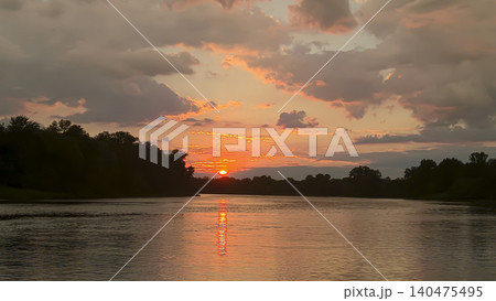 A picturesque sunset over the river with reflections of clouds and silhouettes of trees A picturesque sunset over the river with reflections of clouds and silhouettes of trees 140475495