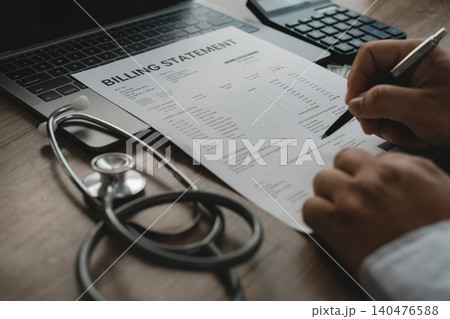 Healthcare professional reviewing a medical billing statement beside a laptop and stethoscope, illustrating healthcare billing, insurance claims verification, medical expense documentation and payment 140476588