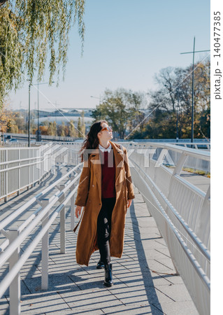 Woman walks on modern pedestrian bridge walkway while looking sideways. Walkable city infrastructure, modern urban pedestrian zone, navigating city architecture, accessible urban environment. Woman walks on modern pedestrian bridge walkway while looking sideways. Walkable city infrastructure, modern urban pedestrian zone, navigating city architecture, accessible urban environment. 140477385