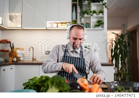 Man enjoying cooking while chopping vegetables in kitchen Man enjoying cooking while chopping vegetables in kitchen 140477471