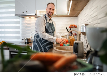 Happy man washing fresh tomatoes in kitchen sink Happy man washing fresh tomatoes in kitchen sink 140477479