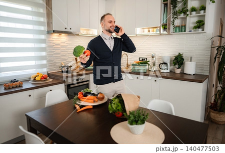 Man talking on phone holding vegetables in kitchen 140477503