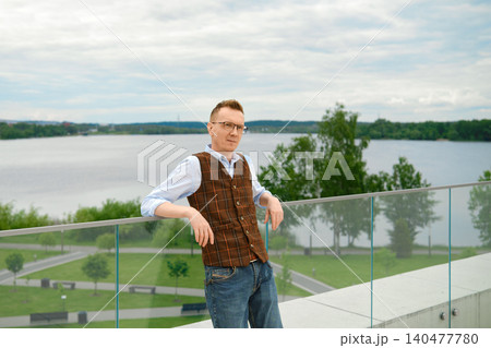 Stylish middle-aged man stands on balcony of observation desk near lake in city park 140477780