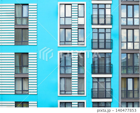 A vibrant blue facade of a contemporary multi-story residential building showcasing a grid of windows and balconies 140477853