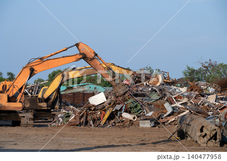 Excavator magnet lifting steel scraps from recycling materials pile at scrap yard in recycling factory. Excavator with electro and magnetic sucker magnet chuck. Special excavator. Scrap metal magnet. Excavator magnet lifting steel scraps from recycling materials pile at scrap yard in recycling factory. Excavator with electro and magnetic sucker magnet chuck. Special excavator. Scrap metal magnet. 140477958