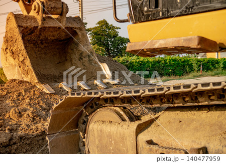 Backhoe parked at construction site after digging soil. Closeup bucket of bulldozer. Digger after work. Earth moving machine at construction site of road repair. Digger with dirt bucket and soil. 140477959
