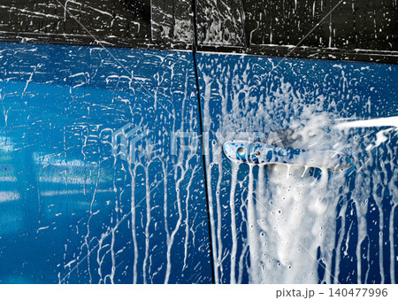 Blue car wash with white soap foam and professional auto care service. Car cleaning service concept. Vehicle cleaning service. Foam wash car detailing. Blue luxury SUV car is covered with white foam. Blue car wash with white soap foam and professional auto care service. Car cleaning service concept. Vehicle cleaning service. Foam wash car detailing. Blue luxury SUV car is covered with white foam. 140477996