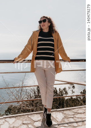 Woman sea viewpoint standing at a coastal lookout wearing a yellow raincoat and sunglasses on a sunny day Woman sea viewpoint standing at a coastal lookout wearing a yellow raincoat and sunglasses on a sunny day 140479279
