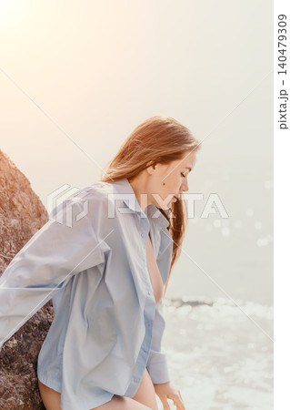 Woman beach shirt sitting on coastal rocks by the sea at sunset with copy space Woman beach shirt sitting on coastal rocks by the sea at sunset with copy space 140479309
