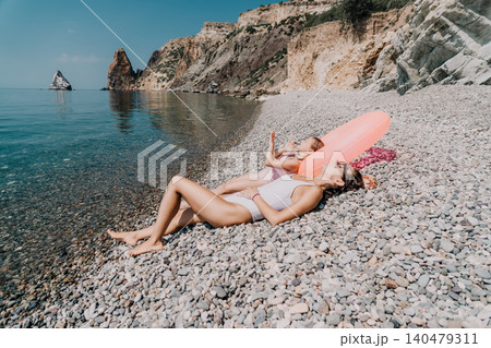 Summer beach vacation woman and child lying on pebble shore by the turquoise sea with mountains in background 140479311
