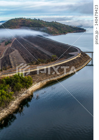 Vertical Aerial view of the Glenbawn Dam wall featuring the water intake system and servicing pontoon with fog floating across the water in NSW Australia. 140479423