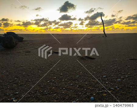 Golden light bathes a quiet beach at sunset. Footprints and driftwood on dark sand evoke feelings of solitude and reflection, making it ideal for spiritual or travelthemed projects. 140479963