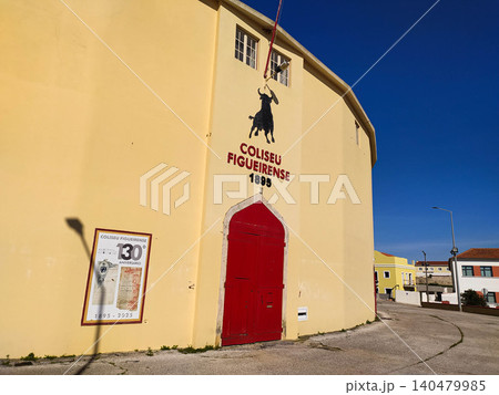 Vibrant yellow facade of a historic Portuguese bullring under a clear blue sky. Features a classic red door and bull emblem, representing Mediterranean culture, tradition, and heritage. Vibrant yellow facade of a historic Portuguese bullring under a clear blue sky. Features a classic red door and bull emblem, representing Mediterranean culture, tradition, and heritage. 140479985