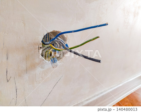 Exposed electrical wires protruding from a socket hole in an unfinished plaster wall during a renovation. Great for home improvement, safety, repair, and DIY construction concepts. Exposed electrical wires protruding from a socket hole in an unfinished plaster wall during a renovation. Great for home improvement, safety, repair, and DIY construction concepts. 140480013