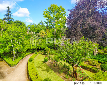 Lush and vibrant manicured European garden featuring winding pathways, sculpted hedges, and a diverse collection of colorful trees under a bright blue sky. Perfect for travel and nature themes. 140480019