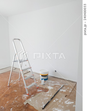 Bright room renovation scene featuring an aluminum stepladder, white paint bucket, and tools on cardboard protecting the floor. Perfect for home improvement and DIY concepts. Bright room renovation scene featuring an aluminum stepladder, white paint bucket, and tools on cardboard protecting the floor. Perfect for home improvement and DIY concepts. 140480033