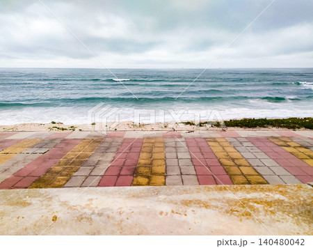 Enjoy a serene coastal view from a colorful tiled promenade overlooking a tranquil blue ocean under a cloudy sky, ideal for travel, wellness, and reflective background designs. Enjoy a serene coastal view from a colorful tiled promenade overlooking a tranquil blue ocean under a cloudy sky, ideal for travel, wellness, and reflective background designs. 140480042