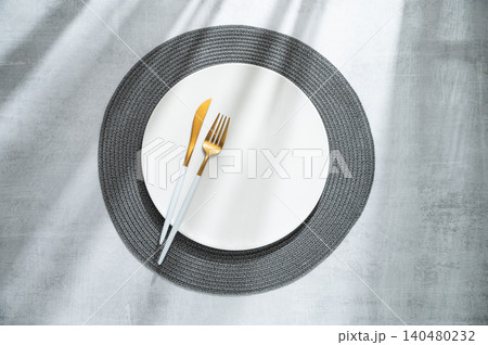 An empty white plate with a fork, knife and dark placemat on a gray concrete background An empty white plate with a fork, knife and dark placemat on a gray concrete background 140480232
