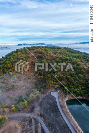 Aerial vertical image of the Glenbawn Dam wall meeting the surrounding mountain landscape surrounded by morning fog in NSW Australia. Drone photograph captures atmospheric low cloud Aerial vertical image of the Glenbawn Dam wall meeting the surrounding mountain landscape surrounded by morning fog in NSW Australia. Drone photograph captures atmospheric low cloud 140480349