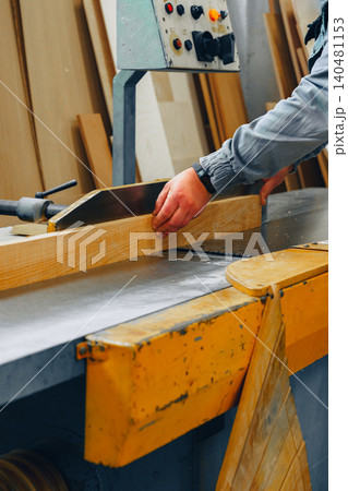 Worker uses machine to shape wood in furniture workshop during daylight hours Worker uses machine to shape wood in furniture workshop during daylight hours 140481153