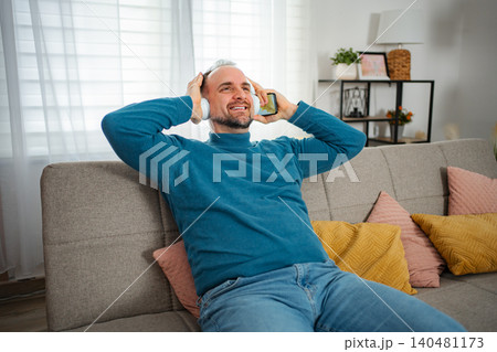 Man relaxing on sofa listening to music with headphones Man relaxing on sofa listening to music with headphones 140481173