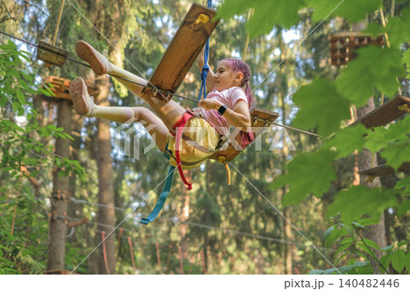 A child fell off the suspension bridge of a rope track with obstacles. Safe passage with safety rope and carbine A child fell off the suspension bridge of a rope track with obstacles. Safe passage with safety rope and carbine 140482446