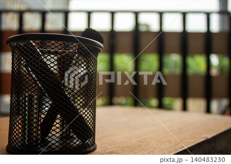 Black Mesh Pen Holder with Makeup Brushes on Wooden Table in Natural Light Black Mesh Pen Holder with Makeup Brushes on Wooden Table in Natural Light 140483230