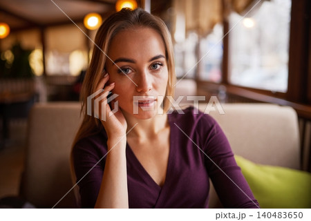 A beautiful blonde woman looking directly at the camera while sitting inside a cozy cafe A beautiful blonde woman looking directly at the camera while sitting inside a cozy cafe 140483650