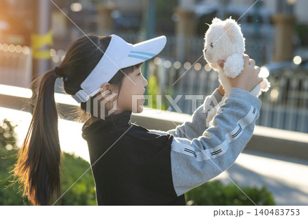 Cheerful little girl playing with teddy bear in park at sunset with golden sunlight 140483753