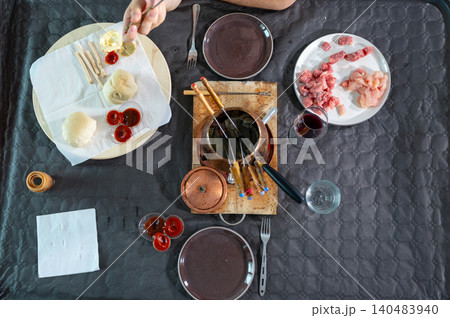 Overhead view of a table set for a meat fondue experience, featuring a bubbling pot of oil surrounded by raw beef and chicken, bread, and different dipping sauces for a gourmet meal Overhead view of a table set for a meat fondue experience, featuring a bubbling pot of oil surrounded by raw beef and chicken, bread, and different dipping sauces for a gourmet meal 140483940