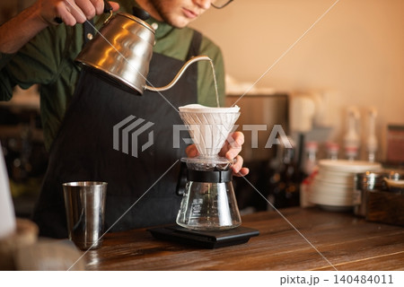 A close up of a barista pouring hot water from a gooseneck kettle into a coffee filter A close up of a barista pouring hot water from a gooseneck kettle into a coffee filter 140484011