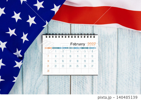 February 2027 monthly desk calendar with United States of America flag on wooden. February 2027 monthly desk calendar with United States of America flag on wooden. 140485139