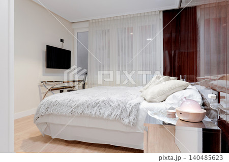 Compact hotel room with double bed and soft textured blanket. Elegant glossy panels and wall-mounted television Compact hotel room with double bed and soft textured blanket. Elegant glossy panels and wall-mounted television 140485623