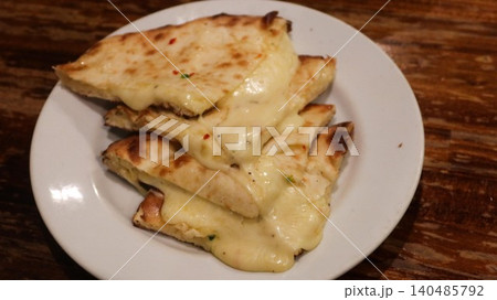 close up of a Indian fusion grilled cheese naan which is a melt creamy cheese stuffed light brown flatbread with herbs and chili flakes on a white plate placed on a rustic wooden table with copy space close up of a Indian fusion grilled cheese naan which is a melt creamy cheese stuffed light brown flatbread with herbs and chili flakes on a white plate placed on a rustic wooden table with copy space 140485792