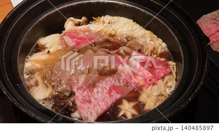 close up of a Japanese sukiyaki hot pot with simmering marbled wagyu beef, mushrooms, Enoki mushrooms, cabbage and tofu in a black pot with copy space 140485897