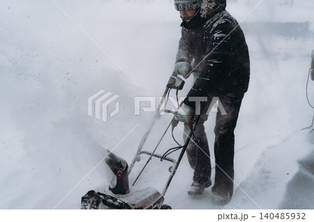 man clearing snowin countryside using electric snow blower 140485932