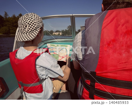 Father and son riding motor boat wearing safety vests having a ride in Neva river, Saint Petersburg Father and son riding motor boat wearing safety vests having a ride in Neva river, Saint Petersburg 140485933