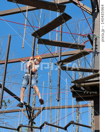 a teenage boy in outdoor rope park passing obstacle course. Active summer holidays a teenage boy in outdoor rope park passing obstacle course. Active summer holidays 140485964