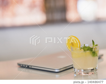 a glass of cocktail and laptop on a bar table a glass of cocktail and laptop on a bar table 140486477
