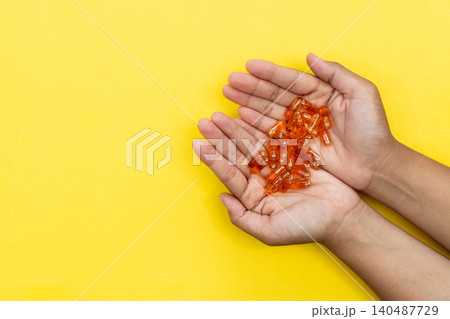 Hands cradle glowing orange capsules against bright yellow background. Soft lighting highlights each pill's glossy texture. Warm tone suggests health, wellness, or self-care Hands cradle glowing orange capsules against bright yellow background. Soft lighting highlights each pill's glossy texture. Warm tone suggests health, wellness, or self-care 140487729