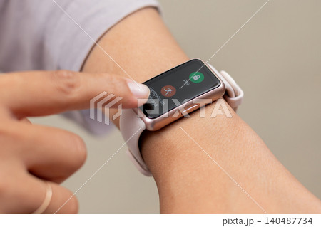 Hand taps smartwatch screen. Finger hovers over call interface. Red button visible. Green option displayed. User engages in real-time decision.  140487734