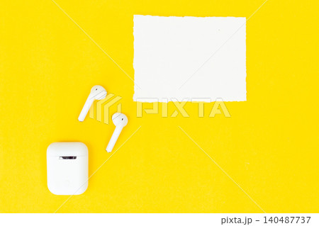 White earbuds rest beside a blank card on bright yellow. Minimalist setup invites creativity or branding. Clean surfaces emphasize modern technology. Perfect for tech, music, or lifestyle visuals White earbuds rest beside a blank card on bright yellow. Minimalist setup invites creativity or branding. Clean surfaces emphasize modern technology. Perfect for tech, music, or lifestyle visuals 140487737