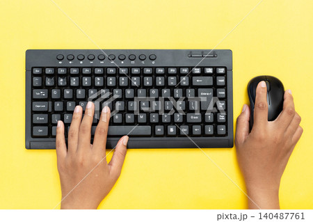 Hands type on black keyboard, mouse clicks beside. Bright yellow background adds cheerful contrast. Fingers move purposefully, suggesting focused work. Ideal for digital tasks, remote learning Hands type on black keyboard, mouse clicks beside. Bright yellow background adds cheerful contrast. Fingers move purposefully, suggesting focused work. Ideal for digital tasks, remote learning 140487761