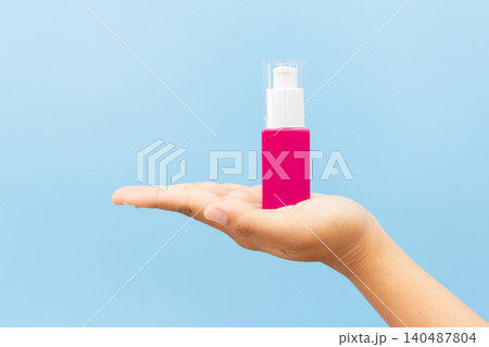 Soft hands hold pink pump bottle. Fingers poised above dispenser, ready to press. Clean background highlights product's simplicity. Ideal for skincare, wellness, or beauty campaigns Soft hands hold pink pump bottle. Fingers poised above dispenser, ready to press. Clean background highlights product's simplicity. Ideal for skincare, wellness, or beauty campaigns 140487804