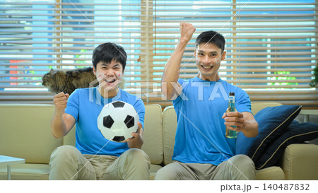 Friends celebrating soccer win at home, mens cheer on sofa after goal 140487832