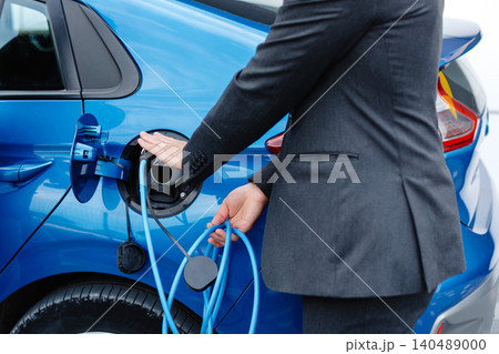 The driver of the electric car inserts the electrical connector to charge the batteries. Unrecognizable man attaching power cable to electric car. The driver of the electric car inserts the electrical connector to charge the batteries. Unrecognizable man attaching power cable to electric car. 140489000