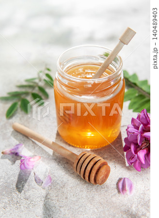 Acacia honey jar on concrete with dipper and flowers Acacia honey jar on concrete with dipper and flowers 140489403